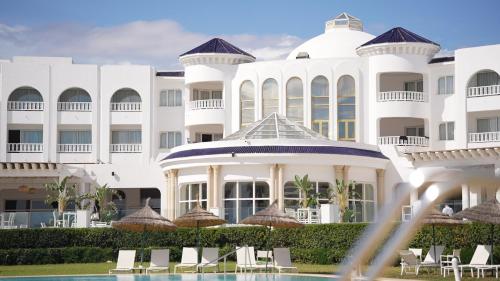 a large white building with chairs in front of it at Royal Tulip Taj Sultan in Hammamet