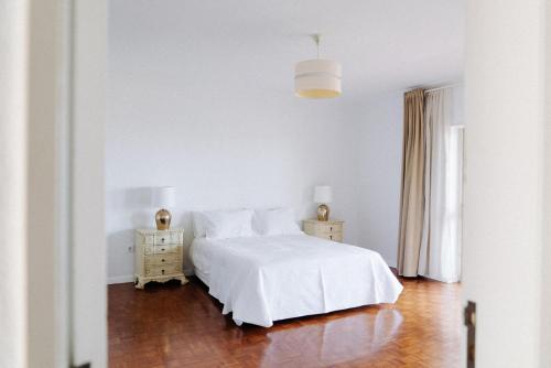 a white bedroom with a white bed and wooden floors at Spacious seaside house in Cascais