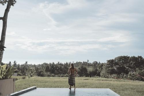 a woman in a striped dress standing on the edge of a patio at SOKO' Stay at Kedungu in Tanah Lot