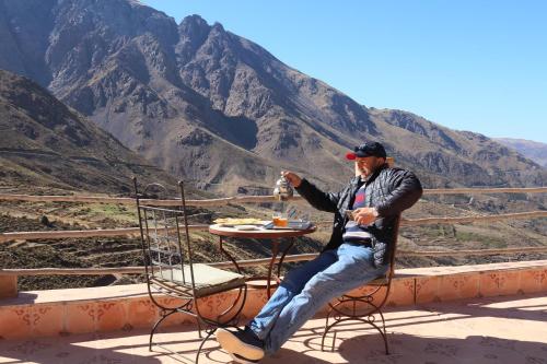 a man sitting at a table in front of a mountain at Gite Ogog Tacheddirt in Tacheddirt