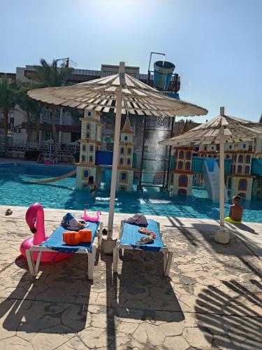 a resort with a pool with two beds and an umbrella at A two-room chalet in the village of Lale Land, Mirage Bay, Ecopark in Hurghada