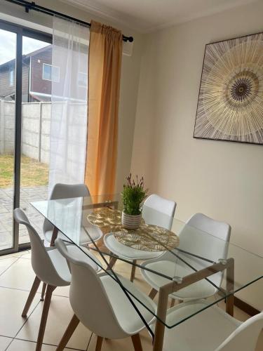 a glass dining room table with white chairs and a plant at Cómoda Casa 4 DORMITORIOS 2 BAÑOS sector Oriente in Talca