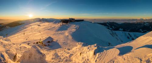 a snow covered mountain with the sun on the horizon at Resort Biela Skala - CHATA Chopok Jasná Juh in Bystrá