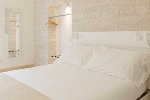 a white bed with white sheets and a white brick wall at Relais La Muraglia - Central Luxury Rooms - Molfetta in Molfetta