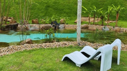 a white chair sitting in front of a pond at Sítio Balango: Seu refúgio em Domingos Martins. Chalés para casais e casa para grupo de pessoas in Domingos Martins