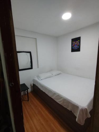 a bedroom with a white bed and a small window at Hostal la 18 in Pereira