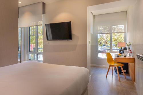 a bedroom with a bed and a desk and a tv at Sercotel El Balcón de la Bahía Suites in Santander