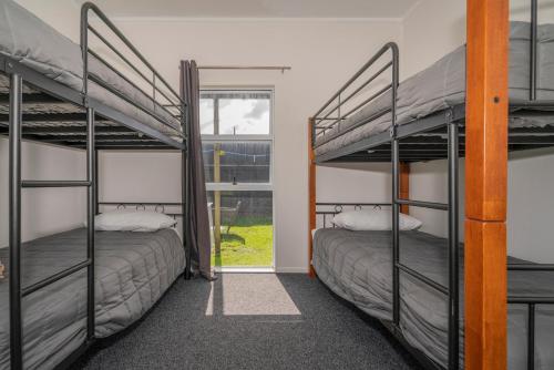 two bunk beds in a room with a window at Across the Road to the Beach - Beach House in Whitianga