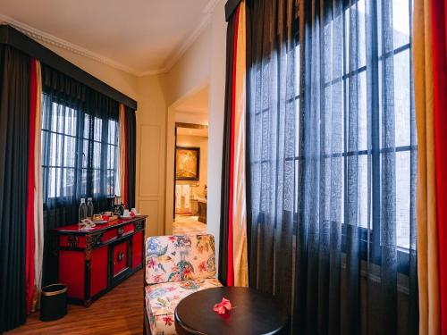 a living room with a chair and a table and windows at House of Tugu, Old Town Jakarta in Jakarta