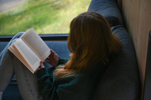 a woman sitting on a couch reading a book at Tiny House Pioneer 3 - Green Tiny Spot Friesland in Schortens