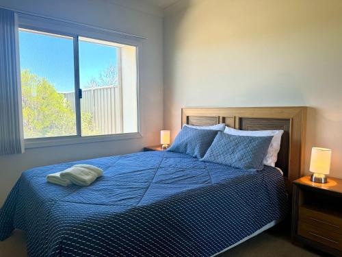 a bedroom with a bed with a blue comforter and a window at Oh Bouy, Unit 62 Seafront Estate in Jurien Bay