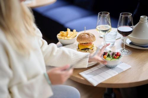 a woman sitting at a table with a hamburger and french fries at C-Hotels Burlington in Ostend