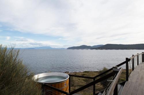 a trash can next to a fence next to a body of water at Siren Tasmania in White Beach