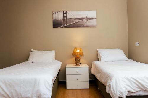 two beds in a room with a lamp on a night stand at STAY In TEHAMA in Cape Town