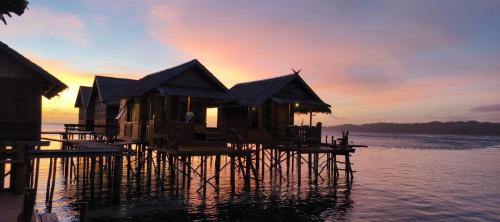 a group of huts on the water at sunset at Happy Homestay Arborek in Besir