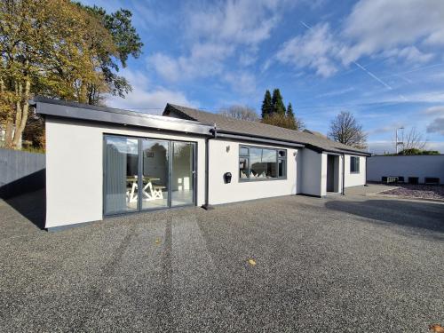a white house with large windows on a driveway at Modern & Spacious 5 Bedroom Bungalow with Parking Near Brecon Beacons & Bike Park Wales in Cefn-coed-y-cymmer
