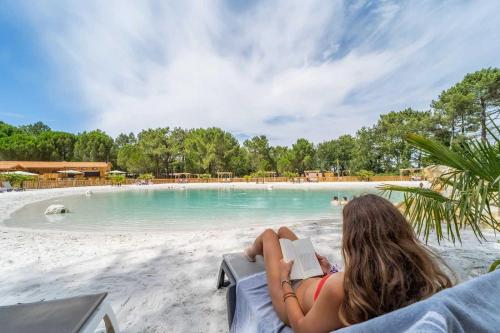 une femme assise sur une chaise en lisant un livre à côté d'une piscine dans l'établissement Camping 4 étoiles - Parc aquatique - ef0bbb, aux Mathes