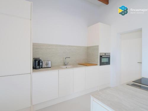 a white kitchen with a sink and a microwave at Sa cova blanca in Cala Pi