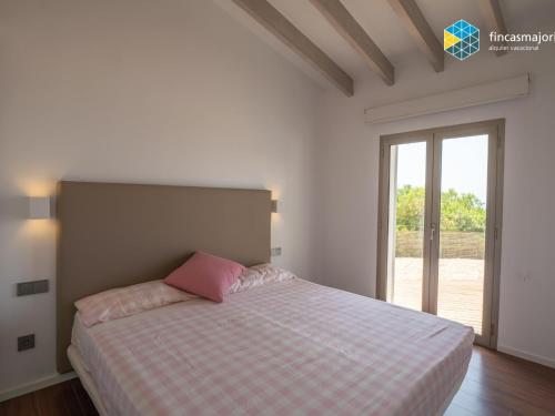a white bedroom with a bed with a pink pillow at Sa cova blanca in Cala Pi