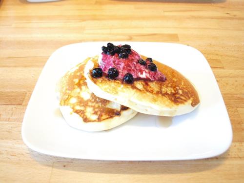 a white plate with two pancakes with berries on it at Chalet Leman by Snow Retreat Catered Chalets in Courchevel