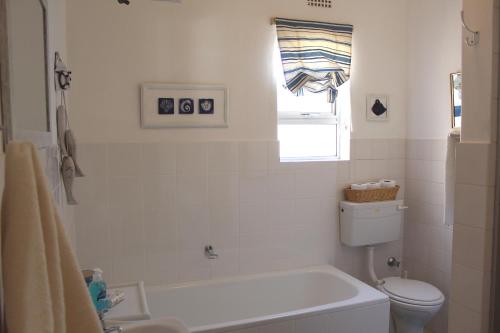 a white bathroom with a tub and a toilet at Beach Haven Cottage in Britannia Bay