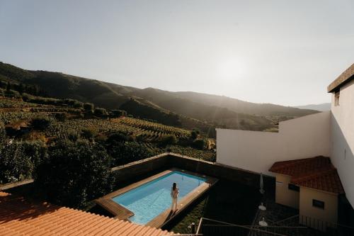 a woman standing in a swimming pool next to a building at Uva Douro Houses in Casais do Douro