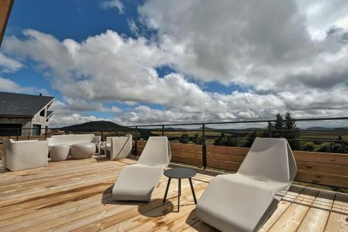 une terrasse en bois avec des chaises blanches et une table dessus dans l'établissement La Flèche 1 - Chalet Standing - Jacuzzi Privatif, à Besse-et-Saint-Anastaise