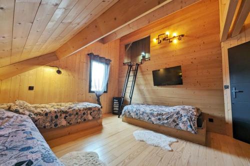 a log cabin bedroom with two beds and a television at La Flèche 2 - Chalet Standing - Jacuzzi Privatif in Besse-et-Saint-Anastaise