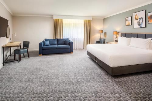 a hotel room with a bed and a blue couch at Delta Hotels by Marriott Milton Keynes in Milton Keynes