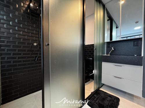 a glass shower door in a bathroom with a brick wall at Get By Side - Jardim Oceania in Tambaú