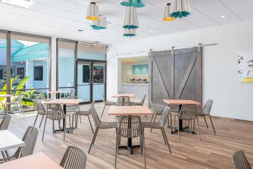 a dining room with tables and chairs and windows at Beachside Hotel & Suites Cocoa Beach - Port Canaveral in Cocoa Beach