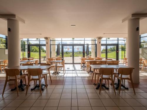 une salle à manger avec tables, chaises et fenêtres dans l'établissement The Originals City, Hôtel des Volcans, à Champs