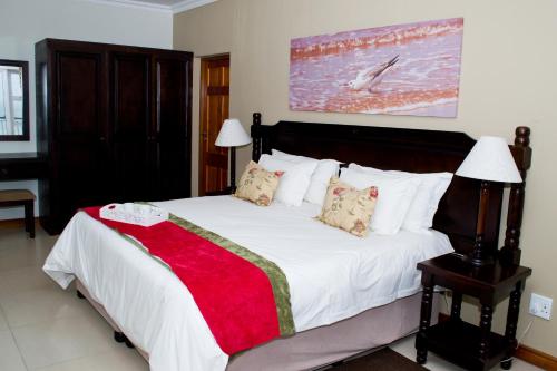 a bedroom with a large white bed with a red blanket at Umthunzi Hotel and Conference in Umtentweni