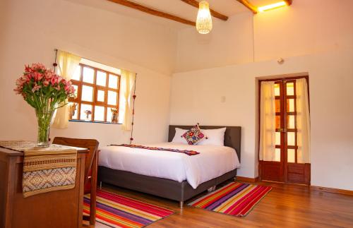 a bedroom with a bed and a vase of flowers on a rug at La Rosa Wellness Lodge in Urubamba