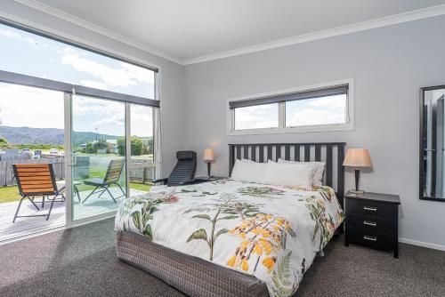 a bedroom with a bed and a balcony with chairs at Hosts on the Coast Belair Bach in Whitianga