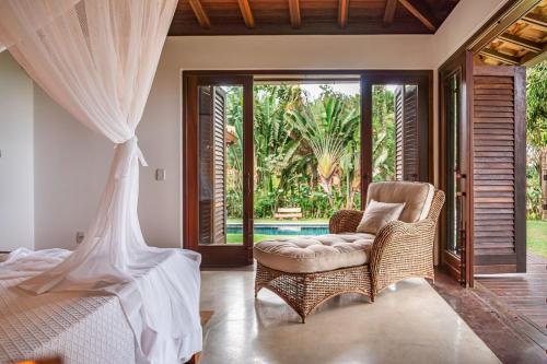 a bedroom with a bed and a chair and a window at Casa Sapucaia Trancoso - Cond. Vale do Segredo in Porto Seguro