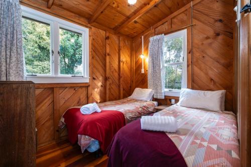 two beds in a room with wooden walls and windows at Quintessential kiwi kuratau bach in Kuratau