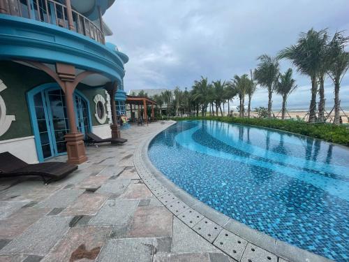 a swimming pool next to a building with palm trees at Ho Tram Beach House in Xuyên Mộc