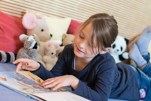 a young girl reading a book in front of stuffed animals at Berggasthof Höchsten in Illmensee