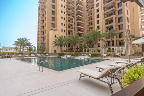 a swimming pool with lounge chairs and buildings at Free housekeeping visits during your stay - StayShort - Warm and Earthy 1-Bedroom Apartment Perfect for Family in Madinat Jumeirah Living! in Dubai