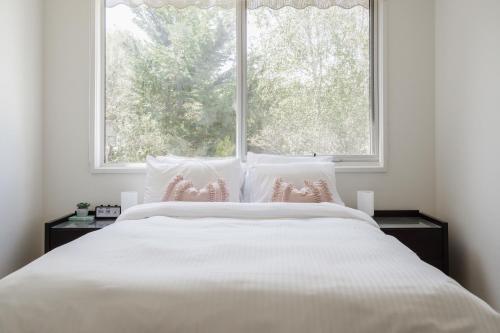 a white bed with pink pillows in front of a window at Treetop Tides - Scenic Tootgarook Coastal Getaway in Tootgarook