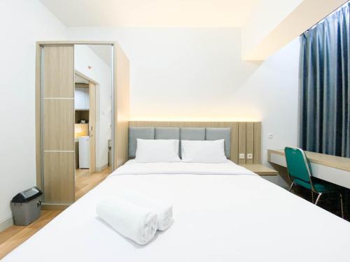 a bedroom with a large white bed and a desk at Comfort and Cozy Stay 1BR at The Alton Apartment By Travelio in Semarang