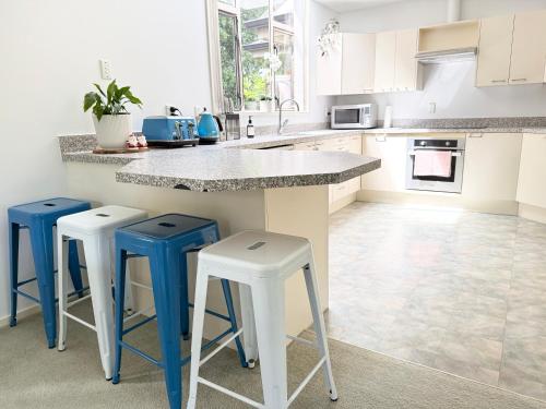 a kitchen with white cabinets and blue stools at Large warm 4BRM family recharge in Halswell - Netflix, Massage chair in Halswell