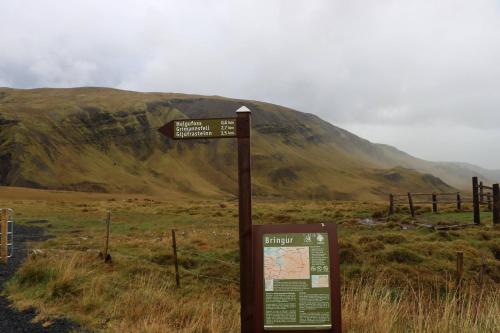 a sign in a field with a mountain in the background at Hlakot Cabin In Golden Circle in Mosfellsbær
