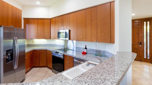 a kitchen with wooden cabinets and a stainless steel refrigerator at ❤PiH❤ Mauna Kea SunsetsOcean and Golf ViewsOptional Mauna Kea Hotel Privileges in Hapuna Beach