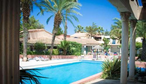 une piscine avec des palmiers et une maison dans l'établissement Lumineux Studio tout équipé, à Canet