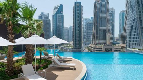a pool with chairs and umbrellas and a city skyline at Jumeirah Living Marina Gate - Golf & Skyline Views with Pool & Gym in Dubai