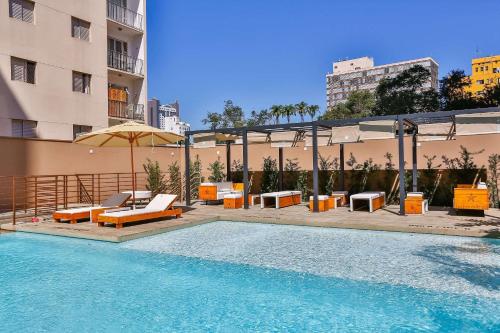 a swimming pool with chairs and an umbrella next to a building at Radisson RED Campinas in Campinas