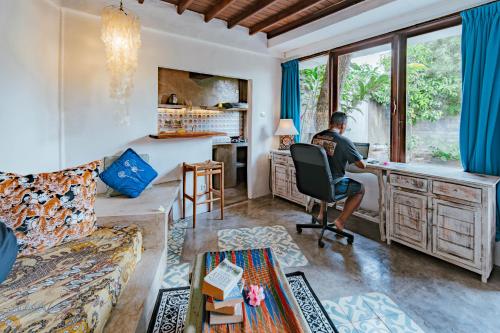 a man sitting in a chair at a desk in a living room at The Onion Collective in Ubud