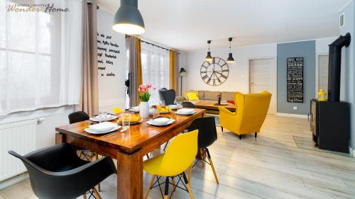 a dining room and living room with a wooden table and yellow chairs at Wonder Home - Domki górskie z kominkami na kameralnym osiedlu - plac zabaw na terenie kompleksu in Karpacz